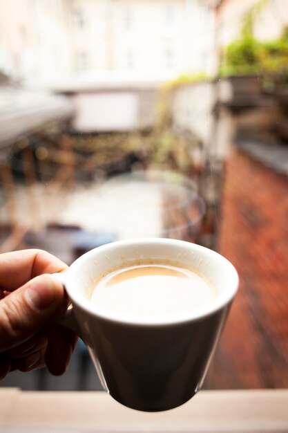 Una mano di persona che tiene tazza di caffè che riflette sul vetro della finestra