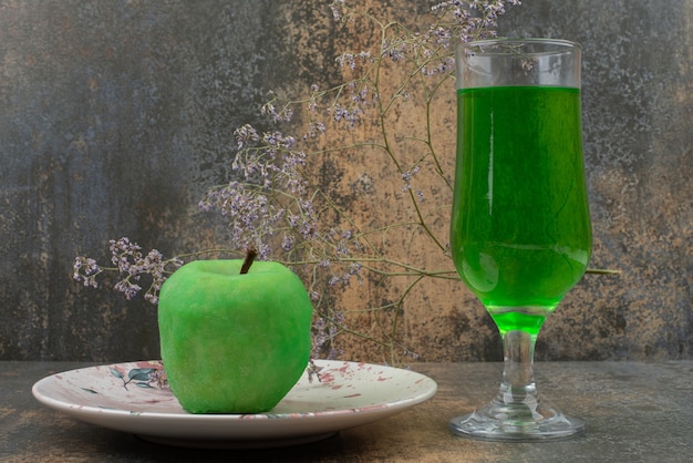 Una mela verde fresca con un bicchiere di acqua verde sul piatto scuro.