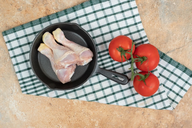 Una padella scura con cosce di pollo e pomodori crudi.