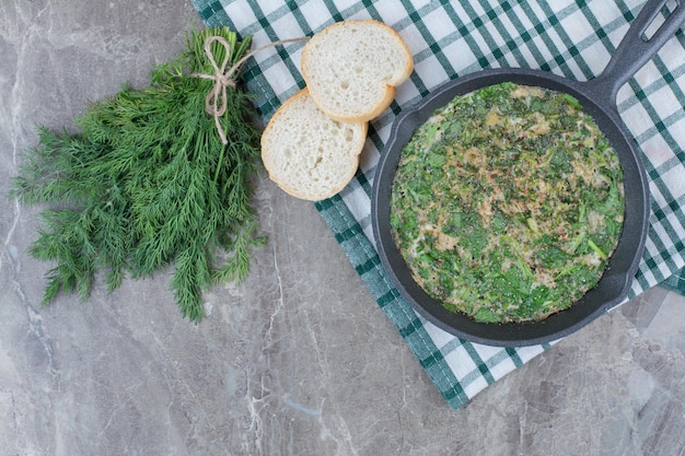 Una padella scura di uova fritte con verdure e pane bianco sulla tovaglia. Foto di alta qualità