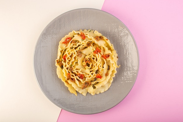Una pasta di pasta vista dall'alto con carne cotta e verdure all'interno della lastra grigia su bianco-rosa