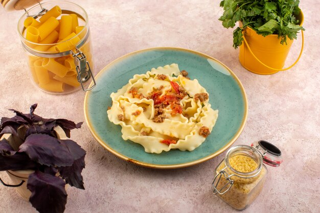 Una pasta di pasta vista dall'alto cucinata gustosa con verdure di carne e salata all'interno di un piatto verde rotondo con fiori e pasta cruda sulla scrivania rosa