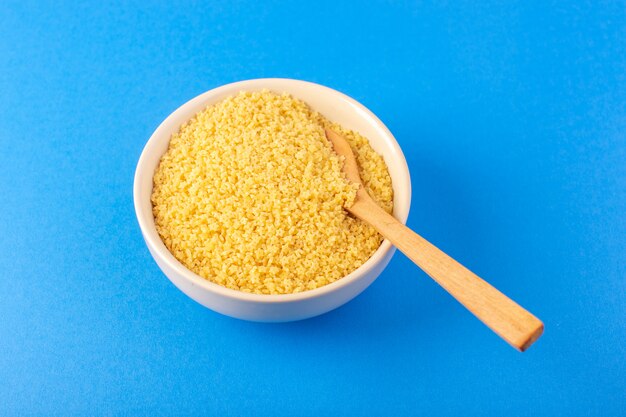 Una pasta gialla cruda di vista superiore dentro la ciotola bianca con il cucchiaio di legno marrone isolato sugli spaghetti blu del pasto dell'alimento del fondo