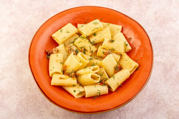 Una pasta italiana con vista dall'alto cucinata gustosa con verdure secche e salata all'interno del piatto rotondo arancione sullo scrittorio rosa