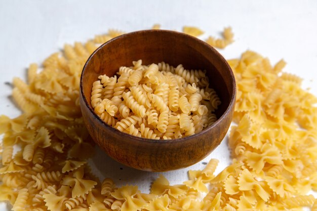 Una pasta italiana cruda di vista frontale poco formata con la zolla marrone sul pasto dell'alimento italiano luminoso della pasta da tavola