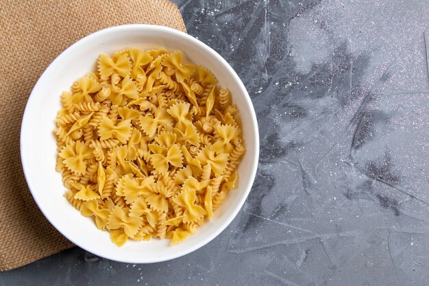 Una pasta italiana cruda di vista superiore poco formata all'interno del piatto bianco sul pasto dell'alimento italiano della pasta grigia dello scrittorio