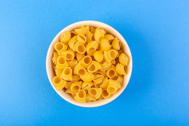 Una pasta secca italia vista dall'alto formava poca pasta cruda gialla all'interno della ciotola rotonda color crema isolata sui precedenti blu pasta italiana dell'alimento degli spaghetti