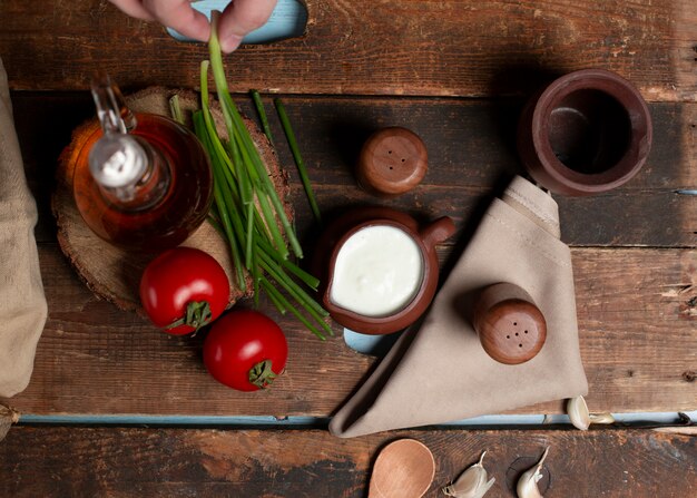 Una pentola di yogurt, pomodori, erbe e bottiglia di oliva sul tavolo di legno Vista dall'alto