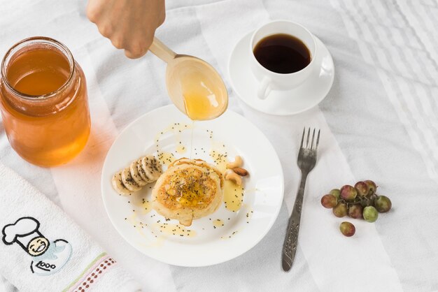 Una persona che aggiunge il miele sul pancake con un cucchiaio di legno