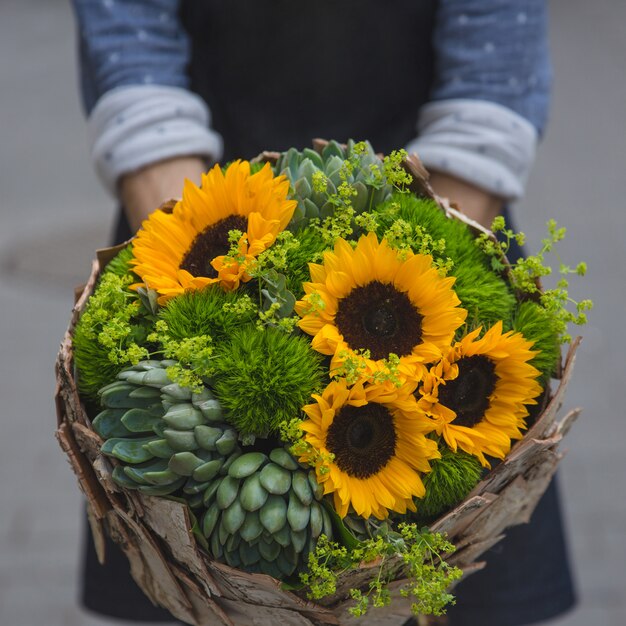 Una persona che offre un bouquet rustico di girasoli e succulente