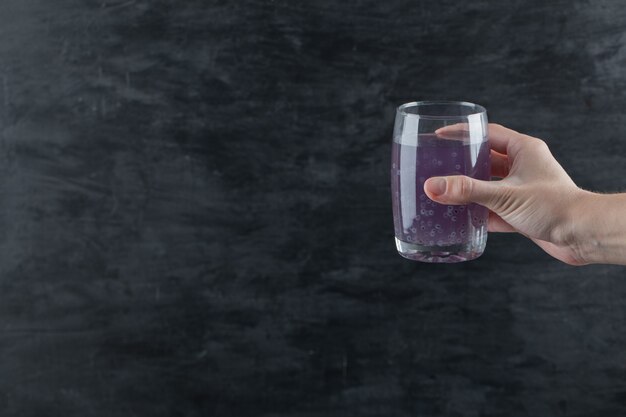 Una persona con in mano un bicchiere di succo viola