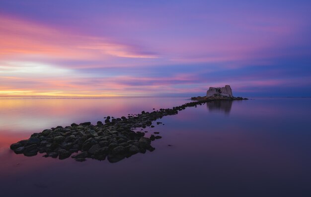 Una piccola isola in mezzo all'oceano sotto un cielo dipinto di molteplici colori