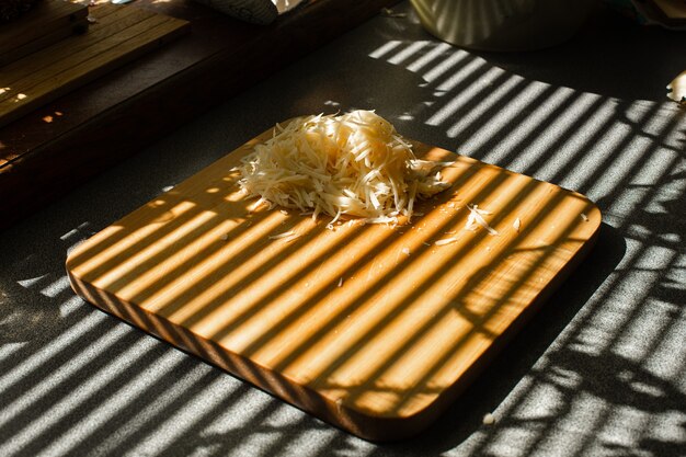 Una piccola pila di formaggio fresco grattugiato giace su una tavola di legno in cucina