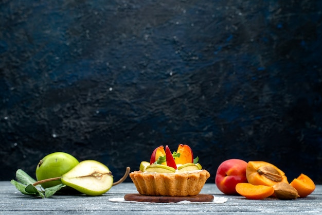 Una piccola torta deliziosa di vista frontale con crema e frutta affettata sul tè grigio del biscotto della torta della scrivania