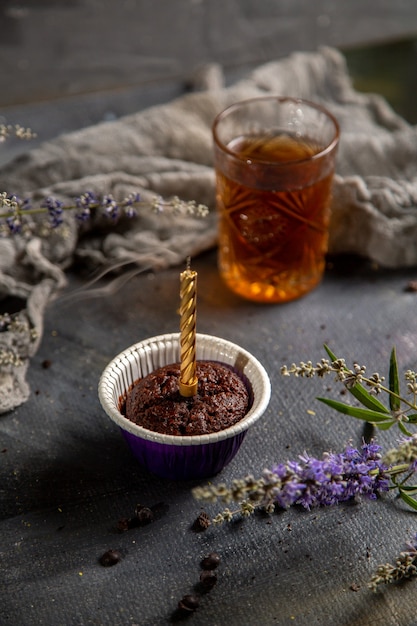 Una piccola torta di cioccolato di vista frontale con la candela ed il tè sul cioccolato grigio della torta del biscotto del biscotto della tavola