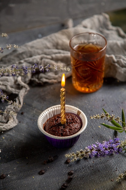 Una piccola torta di cioccolato di vista frontale con la candela ed il tè sul tè grigio del cioccolato della torta del biscotto del biscotto della tavola