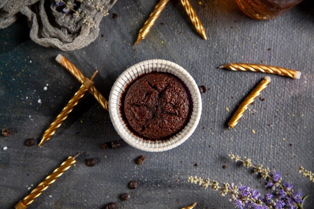 Una piccola torta di cioccolato di vista superiore con i fiori viola delle candele e tè sul tè grigio del cioccolato della torta del biscotto dello scrittorio
