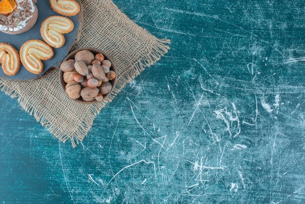 Una piccola torta e biscotti a fiocchi su una tavola accanto a una ciotola di nocciole su sfondo blu. Foto di alta qualità