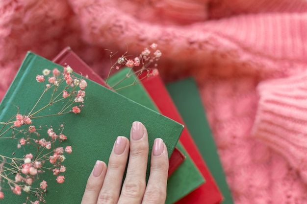 Una pila di libri rossi e verdi con fiori secchi su un maglione lavorato a maglia caldo rosa