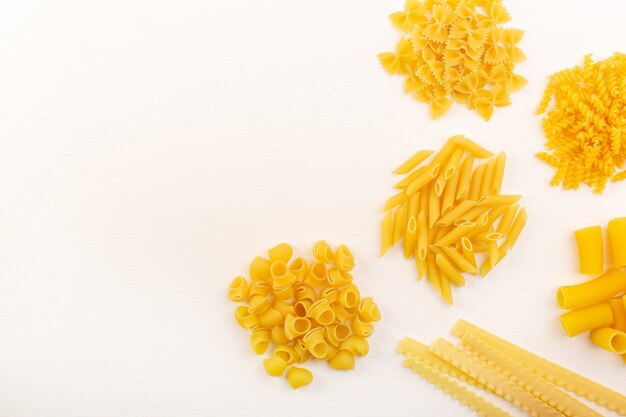Una raccolta di pasta gialla italiana asciutta della pasta cruda di vista superiore e diffusione sul pasto bianco dell'alimento del fondo bianco