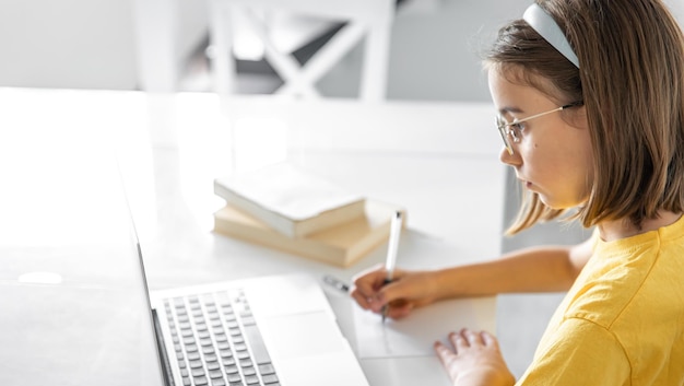 Una ragazza adolescente fa i compiti mentre è seduta con libri e un computer portatile