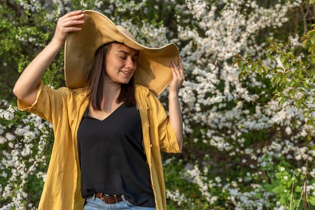 Una ragazza attraente con un cappello tra alberi in fiore gode dell'odore dei fiori primaverili