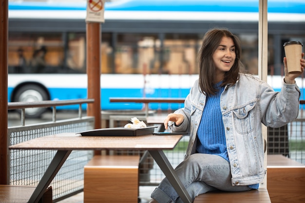 Una ragazza attraente in uno stile casual sta bevendo caffè su una terrazza estiva e sta aspettando qualcuno