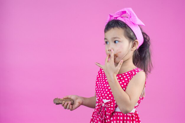 Una ragazza carina che indossa una camicia a strisce rossa che mangia un cioccolato con una bocca sporca sul rosa.