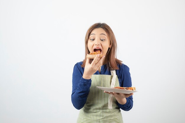 una ragazza carina modella in grembiule che mangia pizza ..