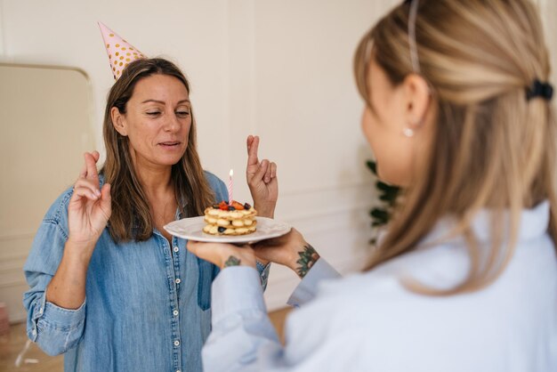 Una ragazza caucasica tiene la torta, un'altra incrocia le dita, spegne la candela ed esprime un desiderio. Concetto di momenti felici