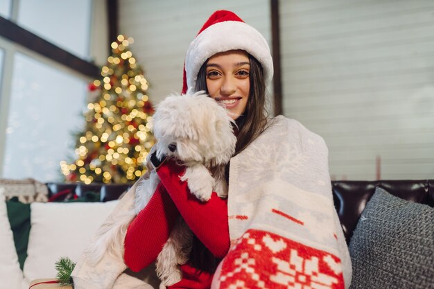 Una ragazza con un cagnolino in braccio si siede sul divano la notte di Capodanno.