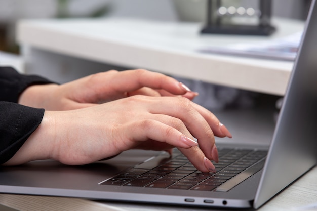 Una ragazza di vista frontale che utilizza computer portatile davanti alla tavola con i programmi e la grafica e che usando attività commerciale di lavoro del computer portatile