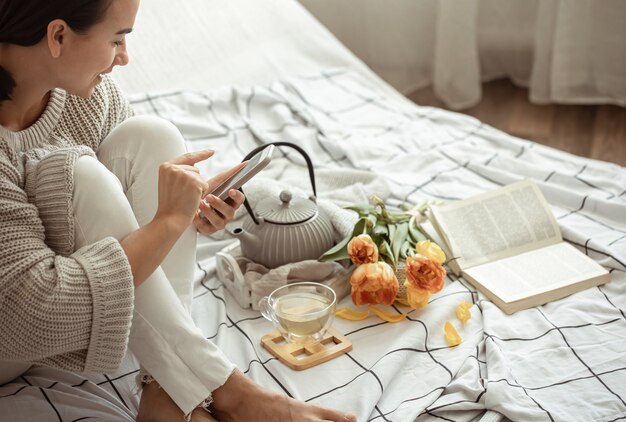 Una ragazza scatta foto sul telefono di una composizione primaverile con tè e tulipani a letto. Concetto di contenuto dei social media.