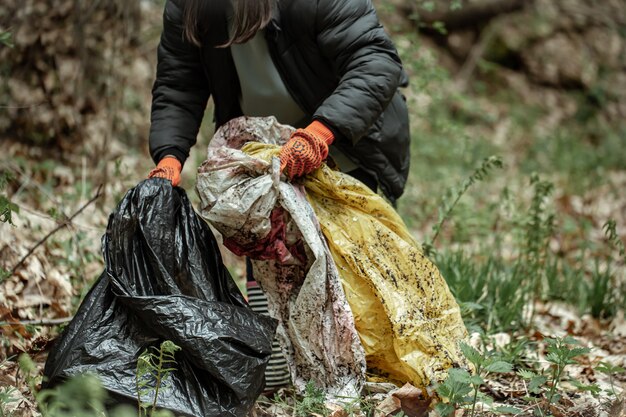 Una ragazza volontaria con un sacco della spazzatura pulisce la spazzatura nella foresta.