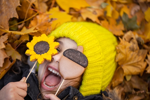 Una ragazzina divertente con un cappello giallo giace nel fogliame autunnale e tiene in mano il pan di zenzero.