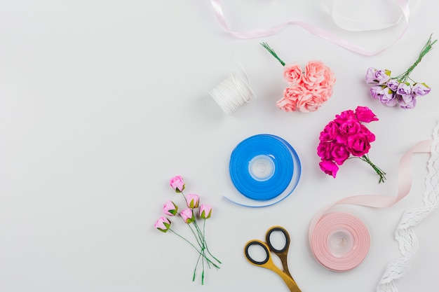 Una rosa artificiale; forbice con nastro blu e rosa su sfondo bianco