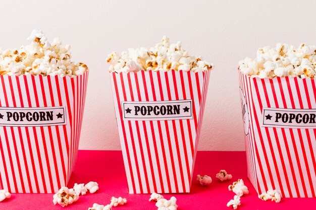 Una scatola di tre popcorn riempita di popcorn su fondo rosa