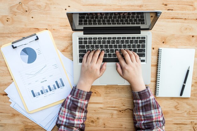 Una scrivania in legno da lavoro (tavola) con computer notebook, tazza di caffè, carta, matita e mano