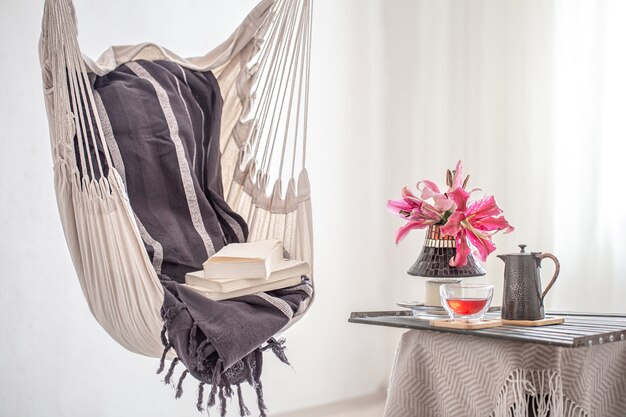 Una sedia pensile in stile boho con libri, teiera e tazza di tè. Il concetto di riposo e comfort domestico.