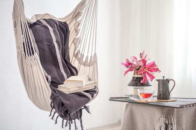 Una sedia pensile in stile boho con libri, teiera e tazza di tè. Il concetto di riposo e comfort domestico.