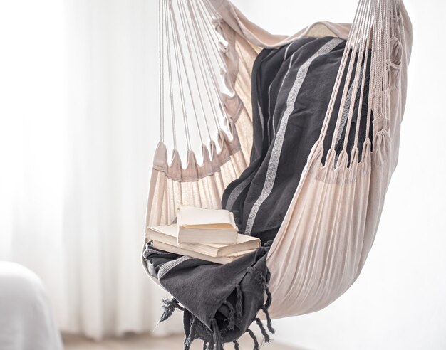 Una sedia pensile in stile boho con una pila di libri. Il concetto di luogo accogliente per rilassarsi a casa.