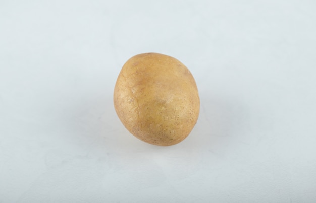 Una singola patata matura cruda su fondo bianco.