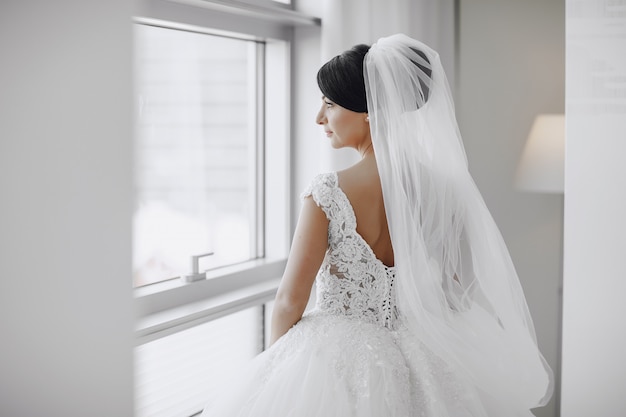 Una sposa elegante e bella a casa in piedi vicino alla finestra