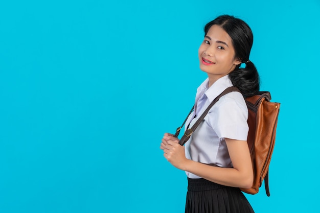 Una studentessa asiatica spia la sua borsa di cuoio marrone su un blu.