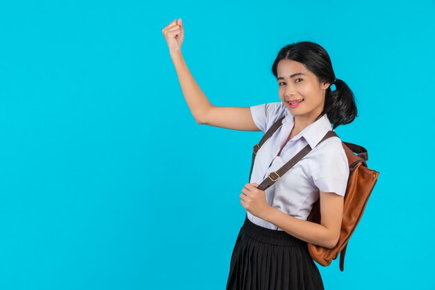 Una studentessa asiatica spia la sua borsa di cuoio marrone su un blu.