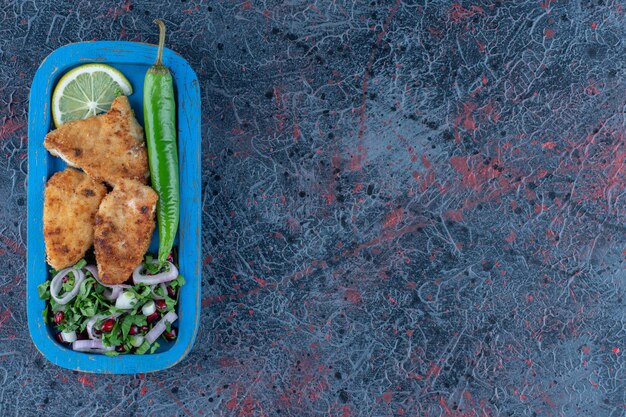 Una tavola di legno blu di cotoletta di pollo al forno con insalata di verdure.