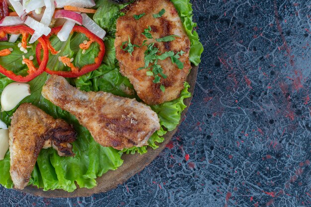 Una tavola di legno con carne di pollo al forno e verdure.