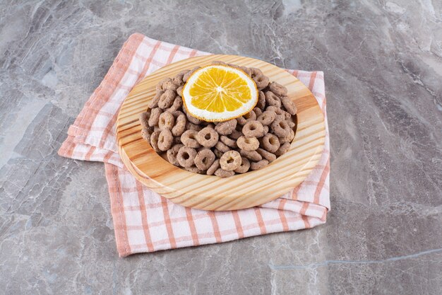 Una tavola di legno di anelli di cereali al cioccolato sani con una fetta di frutta arancione.