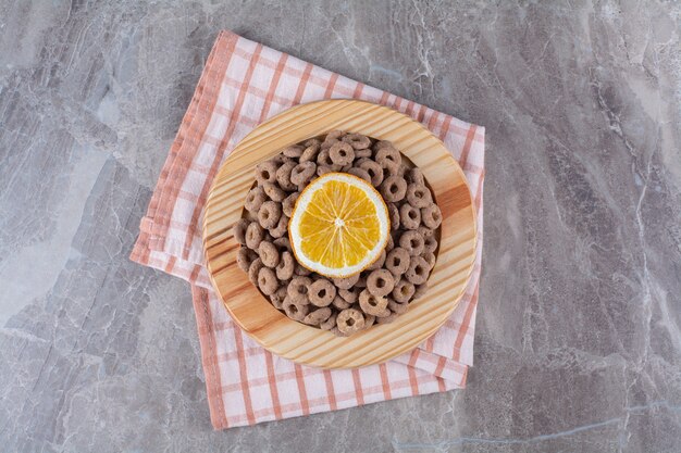 Una tavola di legno di anelli di cereali al cioccolato sani con una fetta di frutta arancione.