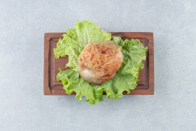 Una tavola di legno di carne di pollo fritto con lattuga.